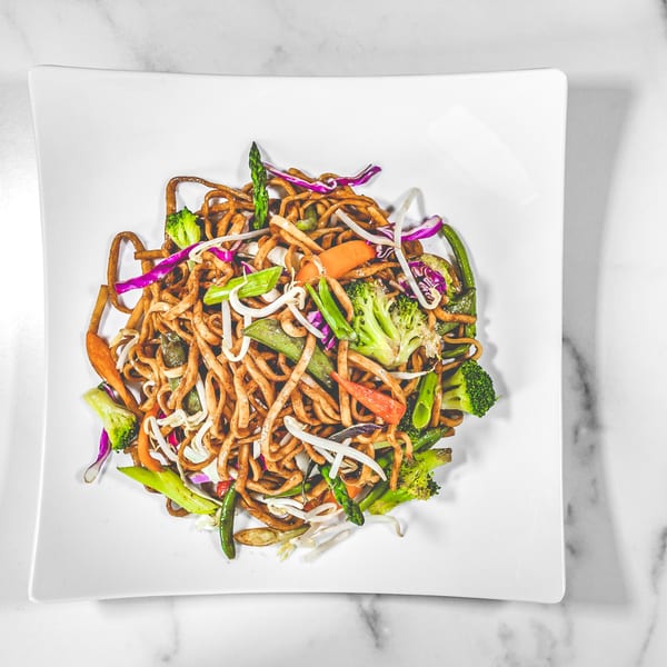 Suzie's Fusion Cuisine's Caribbean stir-fried noodles with colorful vegetables on a white plate.