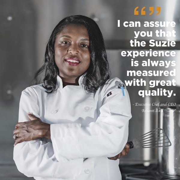 Suzie, the Executive Chef and CEO, in a white chef's coat, holding a spatula.