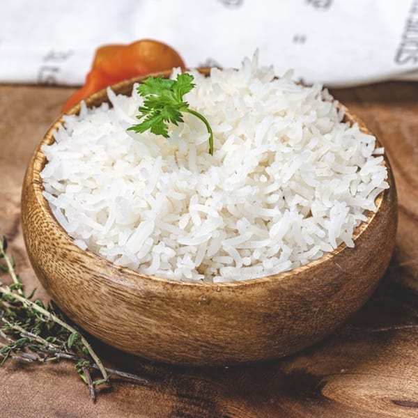 A wooden bowl filled with white rice, garnished with a sprig of fresh parsley.