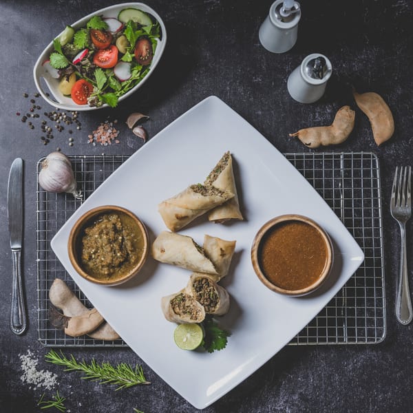 Suzie's Fusion Cuisine Caribbean spring rolls with dipping sauces, salad, and spices on a dark surface.