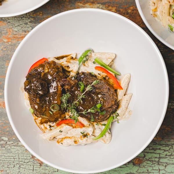 Suzie's Fusion Cuisine's oxtail dish with penne pasta, red bell peppers, and green onions.