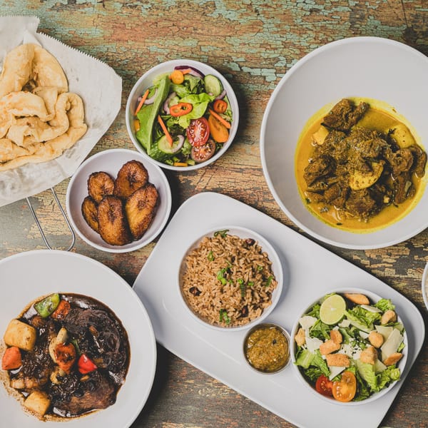A Caribbean feast with curry, stew, rice, plantains, roti, and salads on a rustic wooden table.