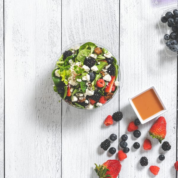 Suzie's Fusion Cuisine berry salad with feta, nuts, and dressing on a white wooden table.