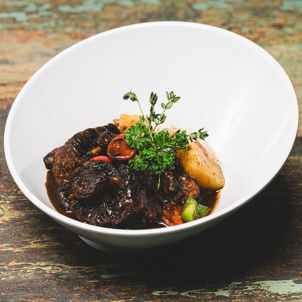 Suzie's Fusion Cuisine's rich Caribbean stew with meat, vegetables, and herbs in a white bowl.