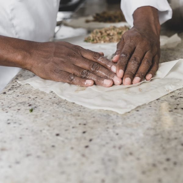 Chef's hands carefully folding Caribbean pastry dough with a savory filling on a granite counter.