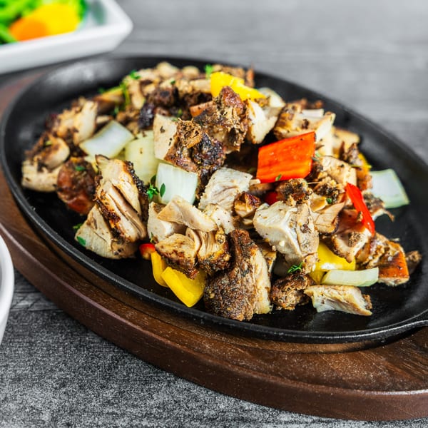 Suzie's Fusion Cuisine's Caribbean jerk chicken with colorful bell peppers and onions on a sizzling platter.