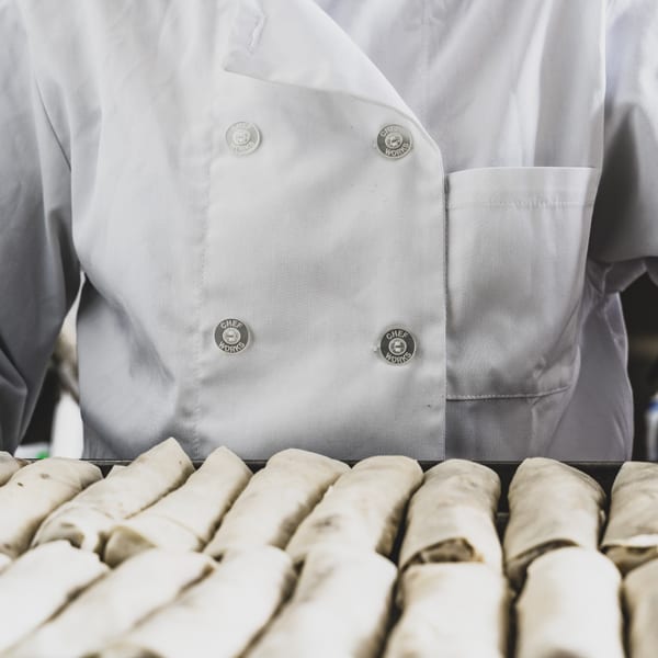 Chef in white uniform preparing Caribbean spring rolls in a professional kitchen.