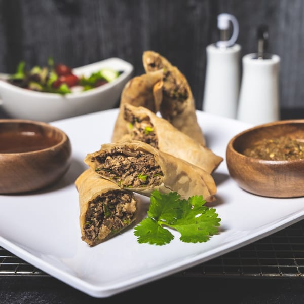 Crispy Caribbean-style spring rolls filled with seasoned meat, served with dipping sauces and a side salad.