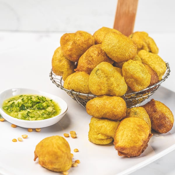 Suzie's Fusion Cuisine's golden fried Caribbean fritters in a wire basket with green dipping sauce.